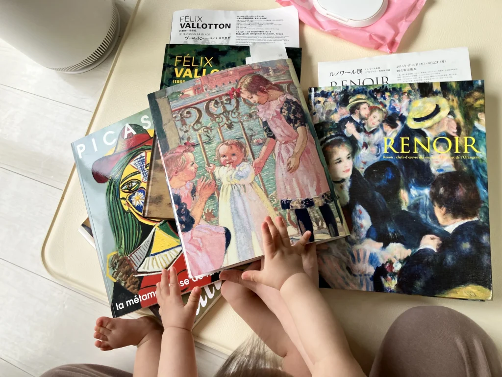 赤ちゃんがピカソやルノワールの画集を触りながらおうちで対話型鑑賞(VTS)をしている様子