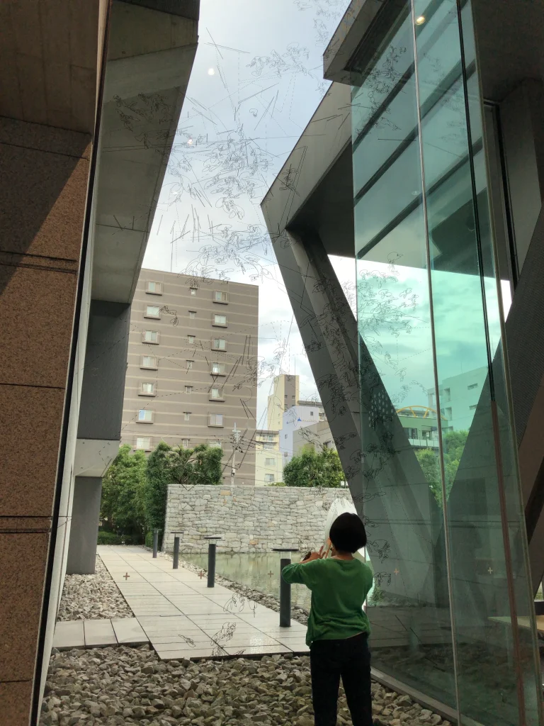 東京都現代美術館のロビーで、画家の文谷有佳里さんがガラス面に直接線を描いている公開制作の様子